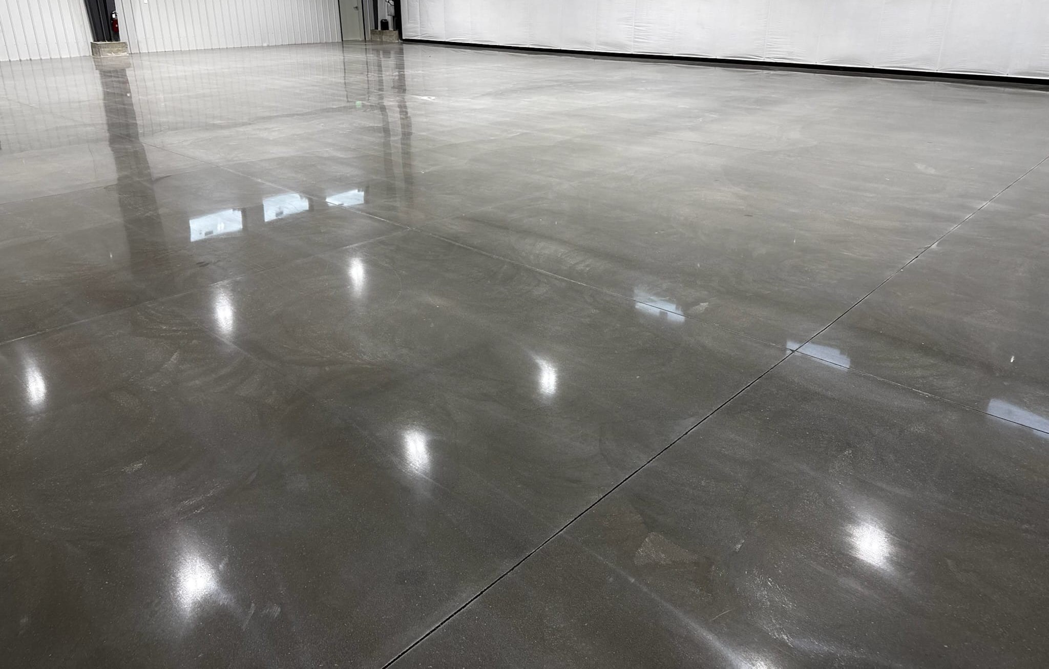 Wide gray polished concrete floor in an open industrial space with rows of ceiling lights reflected across it